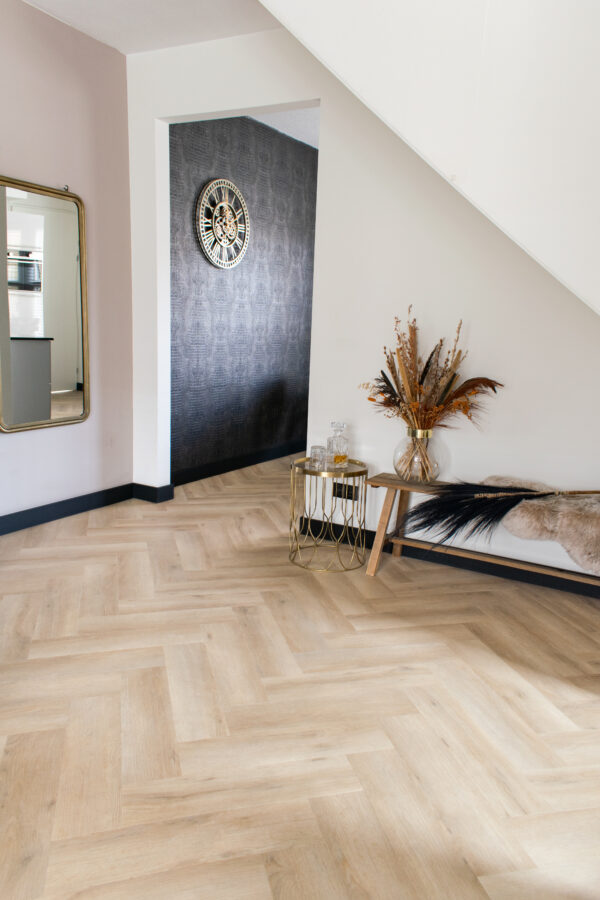 Albendo, vloeren specialist - Een moderne hal met Plak PVC Visgraat Premium Eik Beige - Dryback LV1260V vloeren, een met bont beklede bank, een bijzettafel met gedroogde planten, een grote wandklok en een goudomrande spiegel.