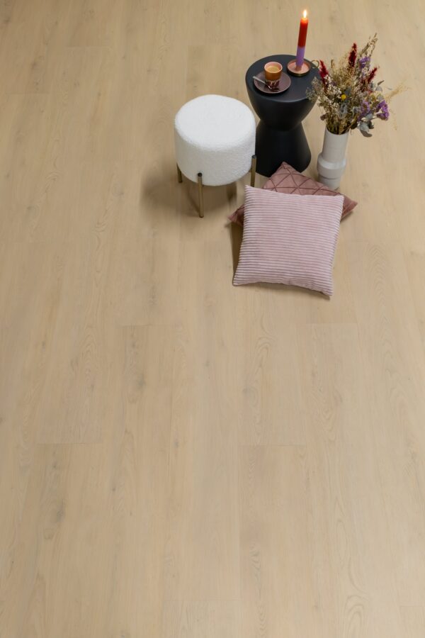 Albendo, vloeren specialist - Een gezellige opstelling op een Plak PVC Beige - Dryback LV1801P vloer met een wit rond krukje, een zwart bijzettafeltje met een brandende kaars en kopjes, een roze kussen en een witte vaas met droogbloemen.