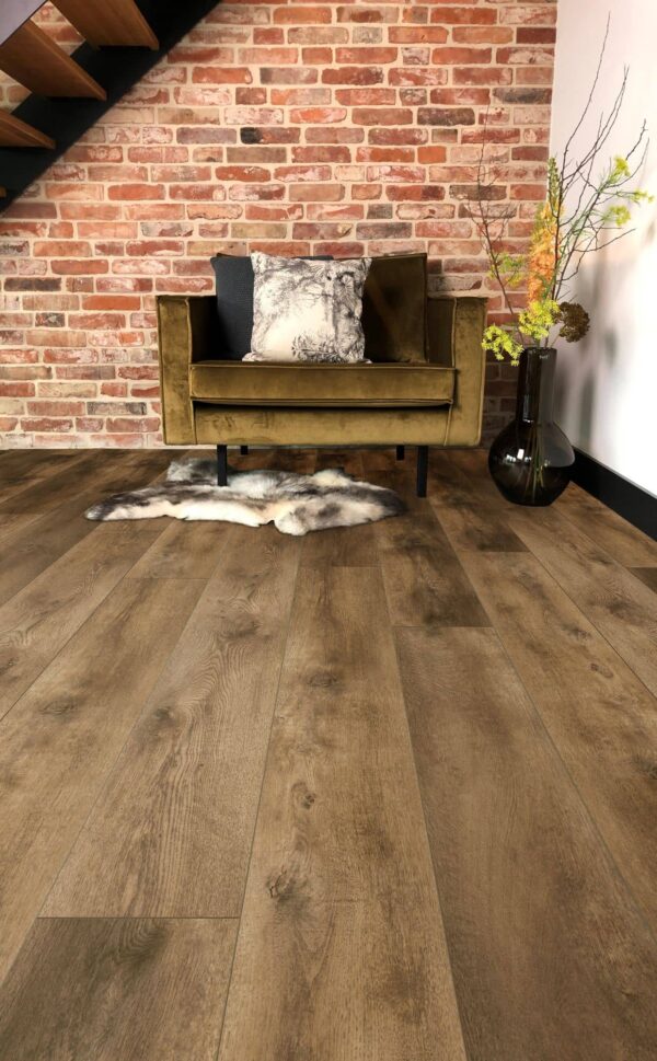 Albendo, vloeren specialist - Een gezellige kamer heeft een mosgroene fluwelen fauteuil, een sierkussen, een vloerkleed van imitatiebont en een vaas met bloemen tegen muren van rode baksteen en Plak PVC Valley Oak Cinnamon - Dryback LV6002P vloeren onder een trap.