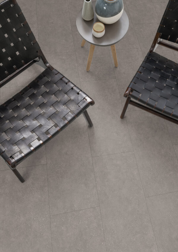 Albendo, vloeren specialist - Twee zwarte geweven leren stoelen staan op de vloer van Waterbestendig Laminaat Stone Beton Grijs, met daartussen een kleine ronde tafel met twee vazen en een schaal.