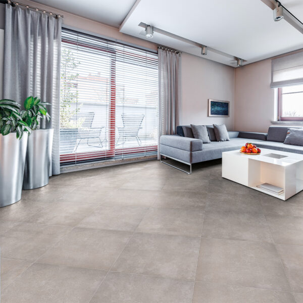 Albendo, vloeren specialist - Moderne woonkamer met grote ramen, Vloertegel / Wandtegel Benelux Light 90x90cm vloertegels, een grijze sectionele bank met kussens, witte salontafel met sinaasappels, planten in potten en gordijnen van vloer tot plafond.