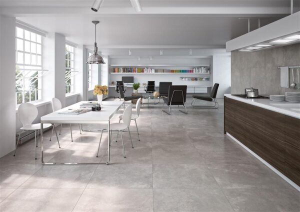 Albendo, vloeren specialist - Modern open kantoor met grote ramen, een vergadertafel met witte stoelen, boekenplanken en een zithoek. De kamer heeft Nexus Antraciet Mat 90x90cm tegels op de vloer en een kitchenette aan de rechterkant.