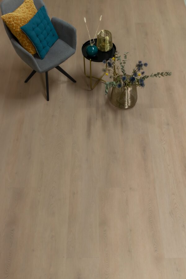 Albendo, vloeren specialist - Een gezellig hoekje met een grijze fauteuil, geel kussen, blauw kussen, ronde tafel met goud decor, koperen vaas met droogbloemen-alles gerangschikt op Click PVC2802 (harde klik) Natural light vloerbedekking.