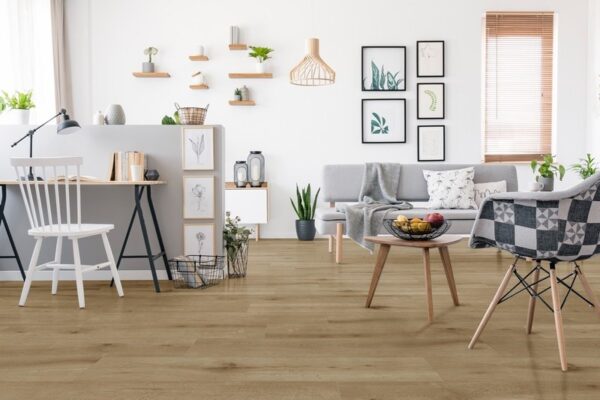 Albendo, vloeren specialist - Een moderne, lichte woonkamer met Click PVC 5102 (harde klik) natuurlijke eiken vloeren, een grijze bank, bureau met witte stoel, potplanten, muurkunst, houten planken en een gezellige stoel gedrapeerd met een deken met patroon.
