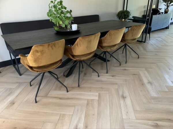 Albendo, vloeren specialist - Een moderne eethoek met een donkerhouten tafel, vier mosterdgele fluwelen stoelen met zwarte poten, een plantenbak en een Click Visgraat 5201 (harde klik) vloer met visgraatmotief in natuurlijk eiken licht.