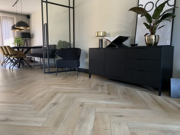 Albendo, vloeren specialist - Moderne woon- en eetkamer met Click Visgraat 5201 (harde klik) Eik natuur licht visgraatvloer, zwarte buffetkast en stoel, planten, minimale inrichting, een eettafel met gele stoelen en een zwarte lamp op de achtergrond.