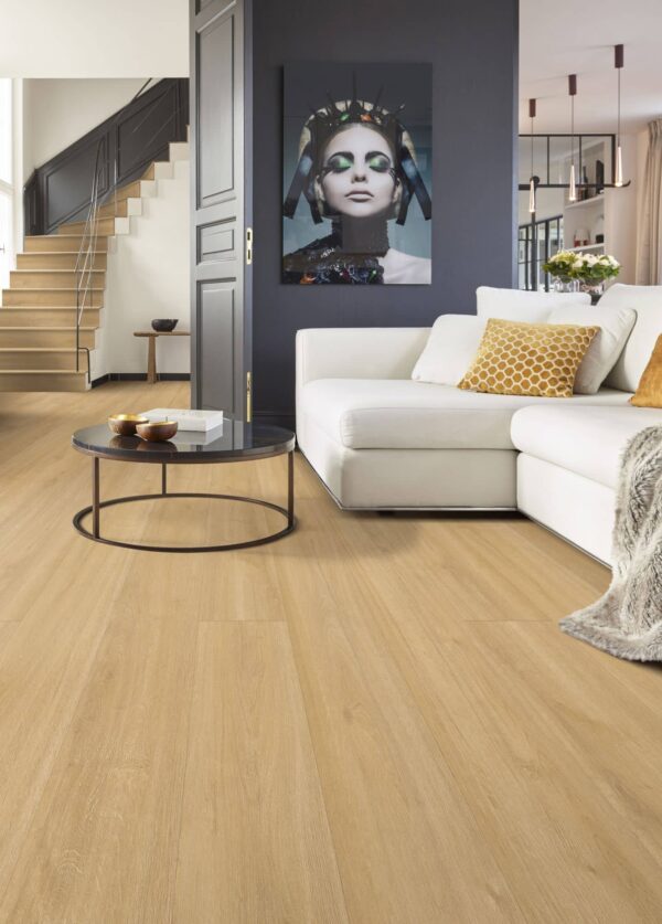 Albendo, vloeren specialist - Een moderne woonkamer met Click PVC 7101 (Rigid Click) Naturel (kopie) vloeren, een witte sofa met kussens met geel patroon, een ronde salontafel, een groot portret op een donkere accentmuur en een zichtbare trap op de achtergrond.