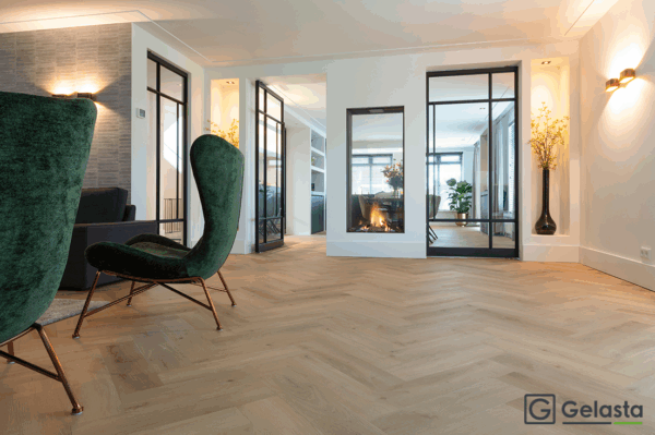 Albendo, vloeren specialist - Moderne woonkamer met Click PVC Visgraat 5400 (Rigid Click) Prestige Oak Natural visgraatvloer, groene fluwelen stoelen, open haard met glazen afsluiting en grote glazen deuren; Gelasta-logo in de hoek.