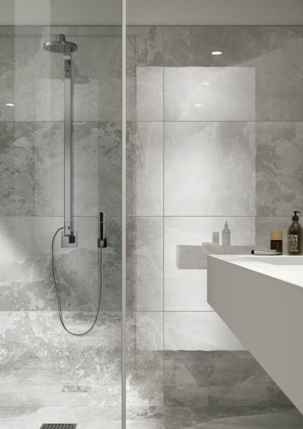 Albendo, vloeren specialist - Moderne badkamer met Kale Hued White 60x120cm wandtegels, een glazen douchewand, strakke chromen douchearmatuur en een wit aanrechtblad met flessen. De algehele look is strak en minimalistisch.